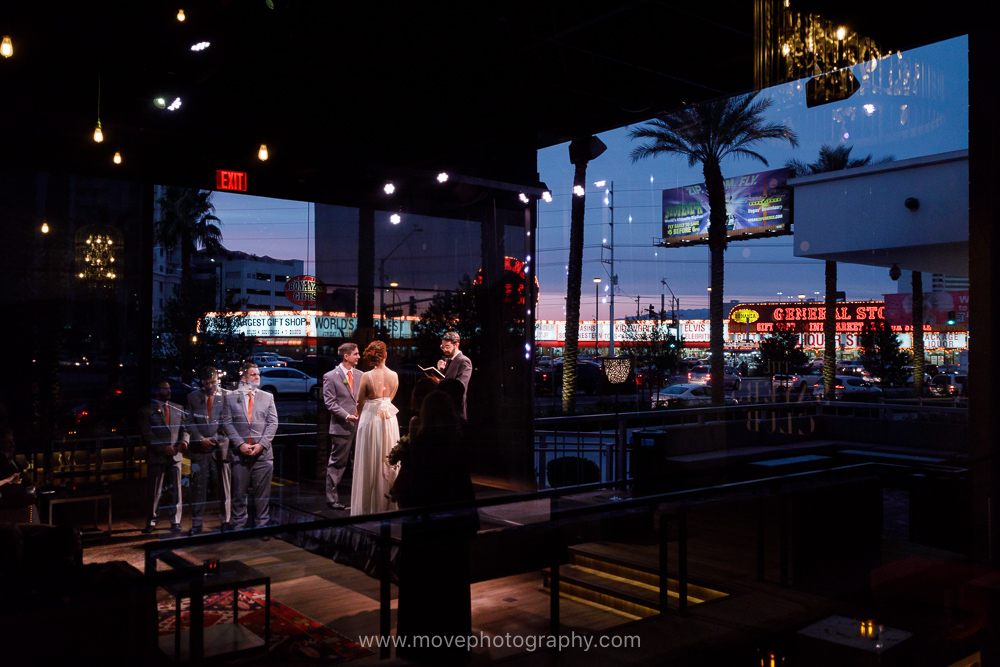 A wedding party stands at the altar at the Sayers Club, in the SLS Las Vegas. Visible in the reflection are the neon lights and marquees of the Las Vegas strip. This SLS Las Vegas wedding took place in the spring. 